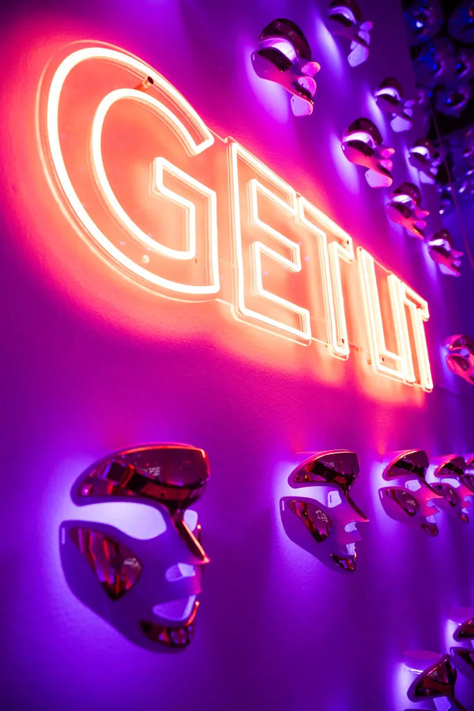 The lounge mask wall with the “Get Lit” neon sign and backlit LED masks