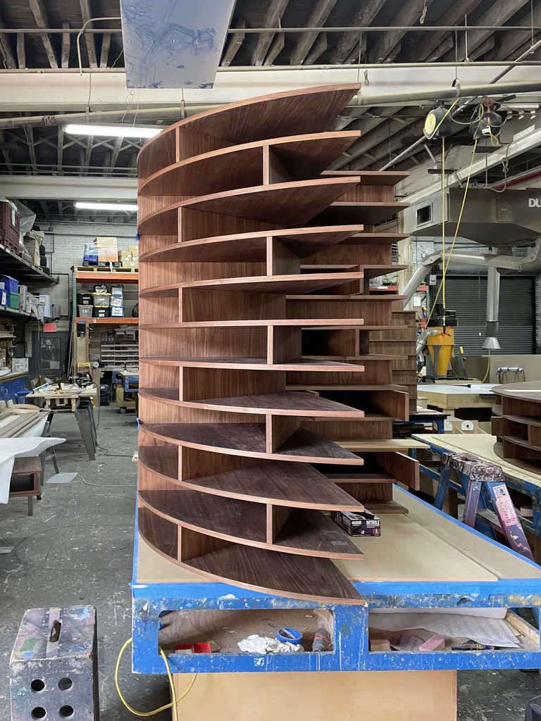 Stacked walnut shelf slabs forming a curved section in the shop