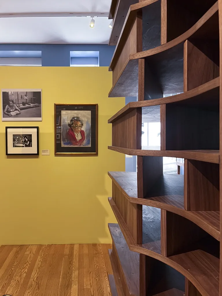 The curved walnut display wall beside a yellow gallery wall of framed portraits